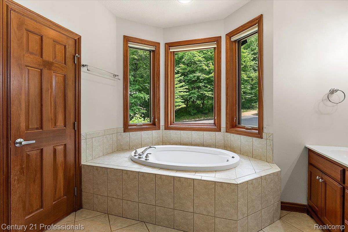 9867 Rainbow Ridge Drive Schoolcraft, MI 49087 - Photo 34 of 82 Soaking tub with a tiled surround, three large windows with wood-finish frames, and a solid wood paneled door