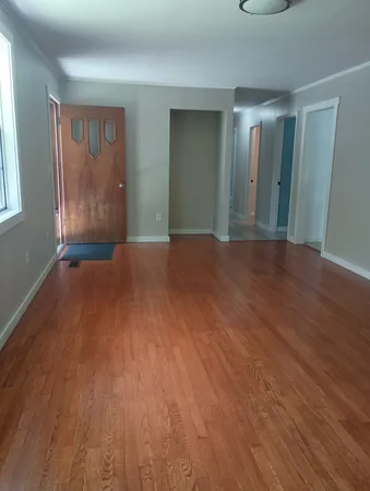 a view of an empty room with wooden floor and window
