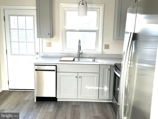 a kitchen with stainless steel appliances a sink cabinets wooden floor and a window