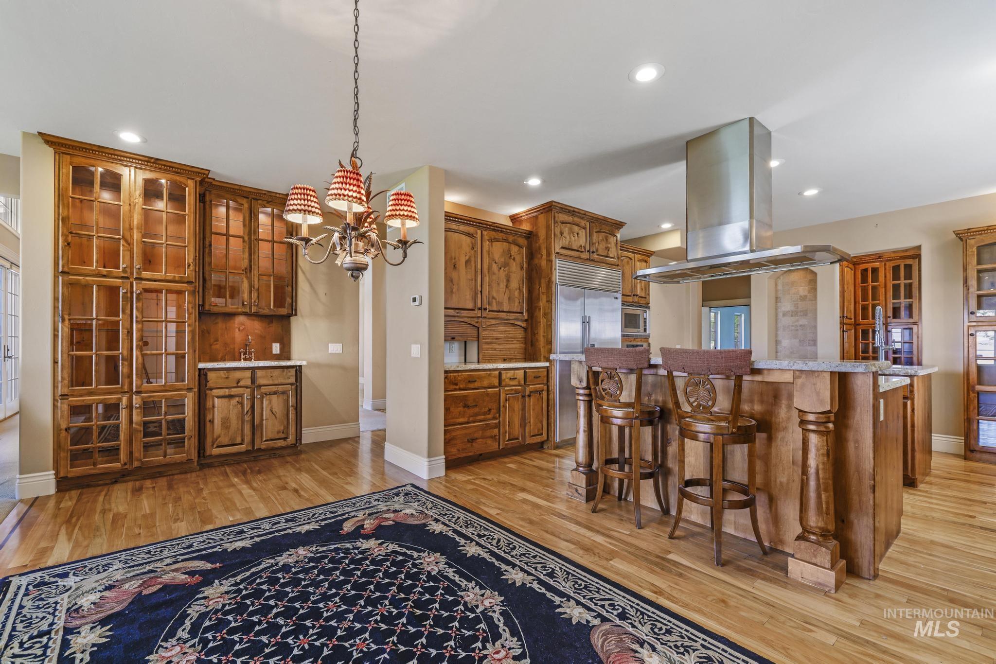 1526 Highway 26 Gooding, ID 83330 - Photo 14 of 48 Kitchen featuring brown cabinets, a kitchen breakfast bar, island exhaust hood, glass insert cabinets, and light wood-type flooring
