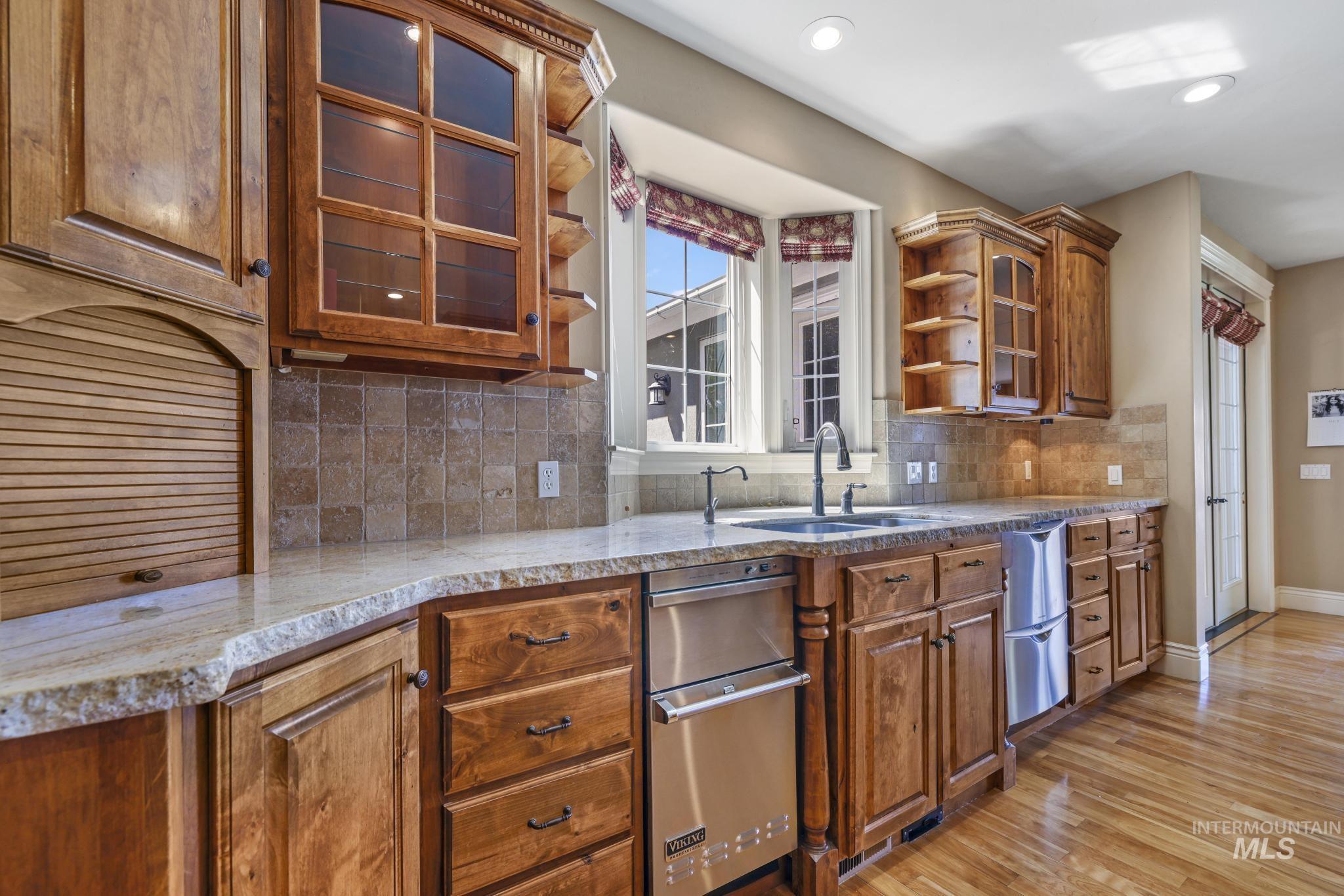 1526 Highway 26 Gooding, ID 83330 - Photo 17 of 48 Kitchen featuring glass insert cabinets, brown cabinetry, tasteful backsplash, light wood-style floors, and light stone countertops