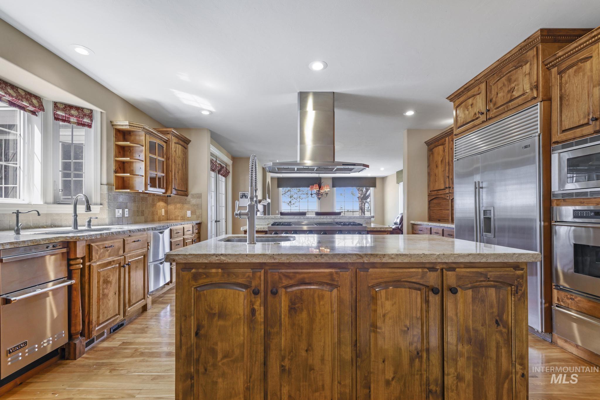 1526 Highway 26 Gooding, ID 83330 - Photo 18 of 48 Kitchen featuring a kitchen island with sink, brown cabinetry, light stone countertops, built in appliances, and light wood-style floors