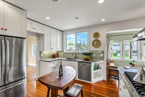 a kitchen with stainless steel appliances granite countertop a stove top oven a refrigerator a dining table and chairs with wooden floor