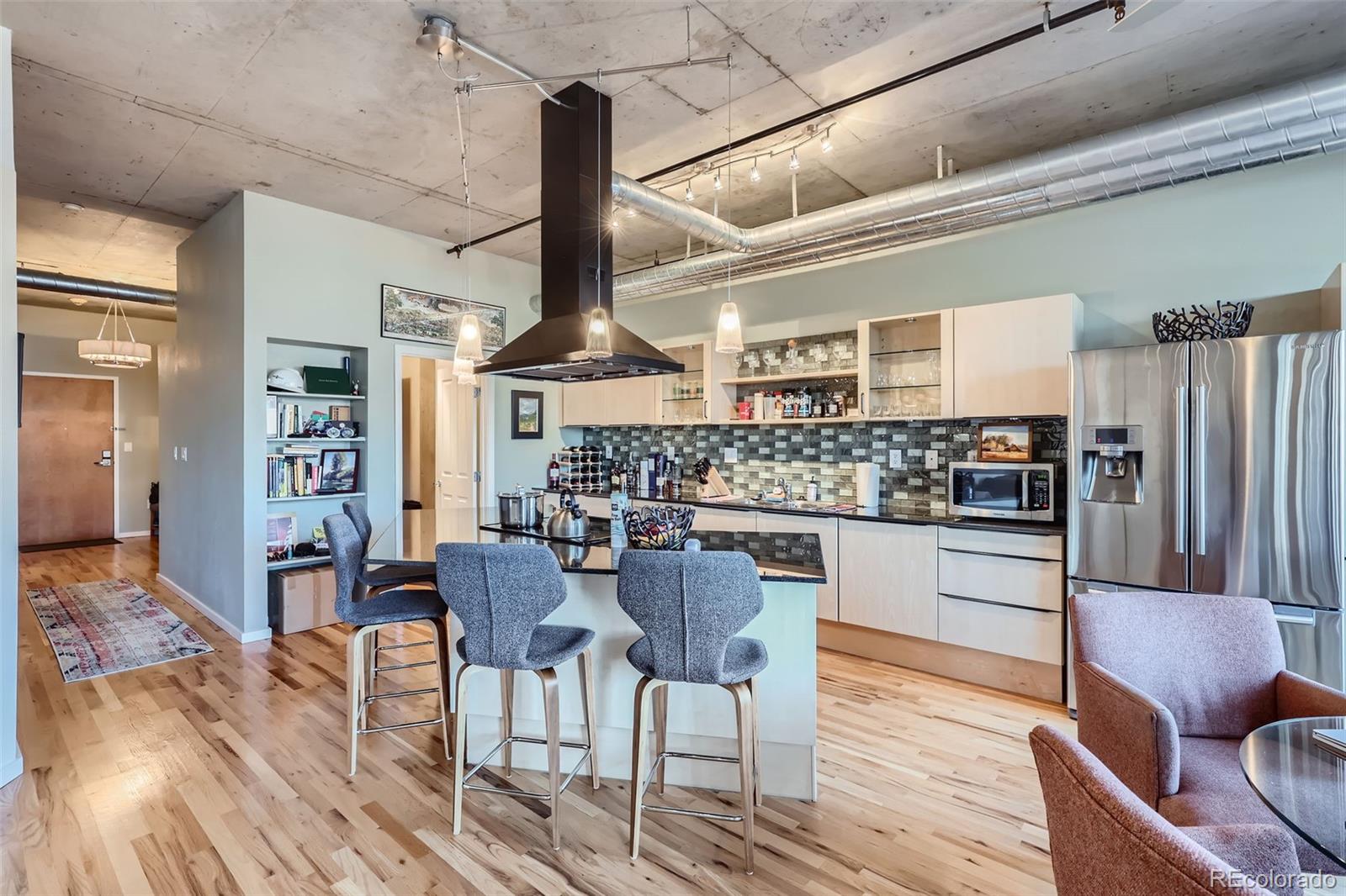 1499 Blake Street, Unit 5I Denver, CO 80202 - Photo 9 of 28 a kitchen with stainless steel appliances kitchen island granite countertop a table chairs and wooden floor
