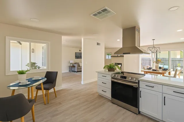 a open kitchen with stainless steel appliances granite countertop a stove top oven a sink dishwasher a dining table and chairs with wooden floor