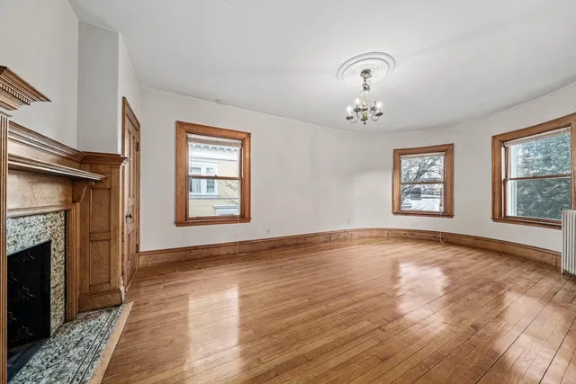 a view of an empty room with wooden floor fireplace and a window