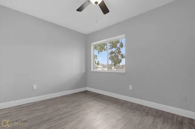 an empty room with wooden floor ceiling fan and window