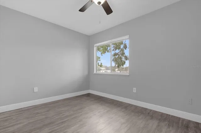 an empty room with wooden floor ceiling fan and window