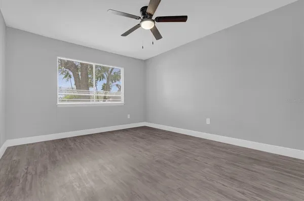 an empty room with wooden floor ceiling fan and windows