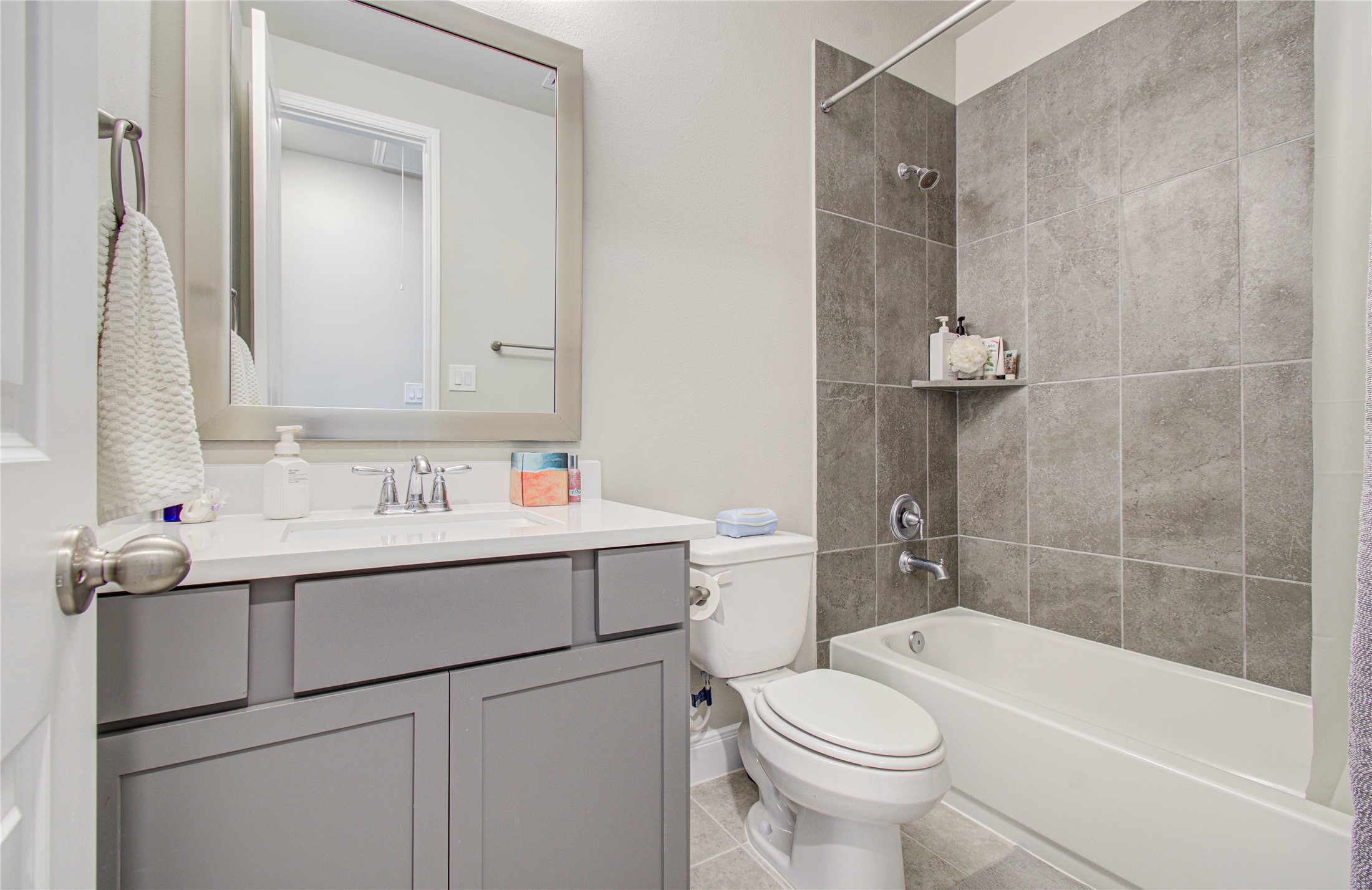 17344 Grand Canyon Road Conroe, TX 77302 - Photo 8 of 49 Modern bathroom with sleek design, featuring a gray vanity, large mirror, and a bathtub with stylish gray tile surround. Clean and bright with contemporary fixtures.