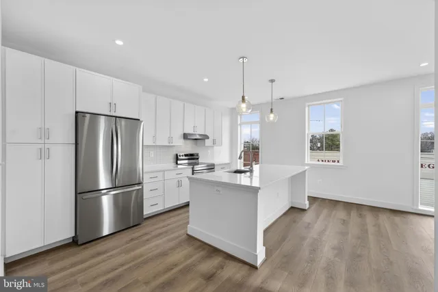 a kitchen with stainless steel appliances a refrigerator a sink dishwasher a stove and white cabinets with wooden floor