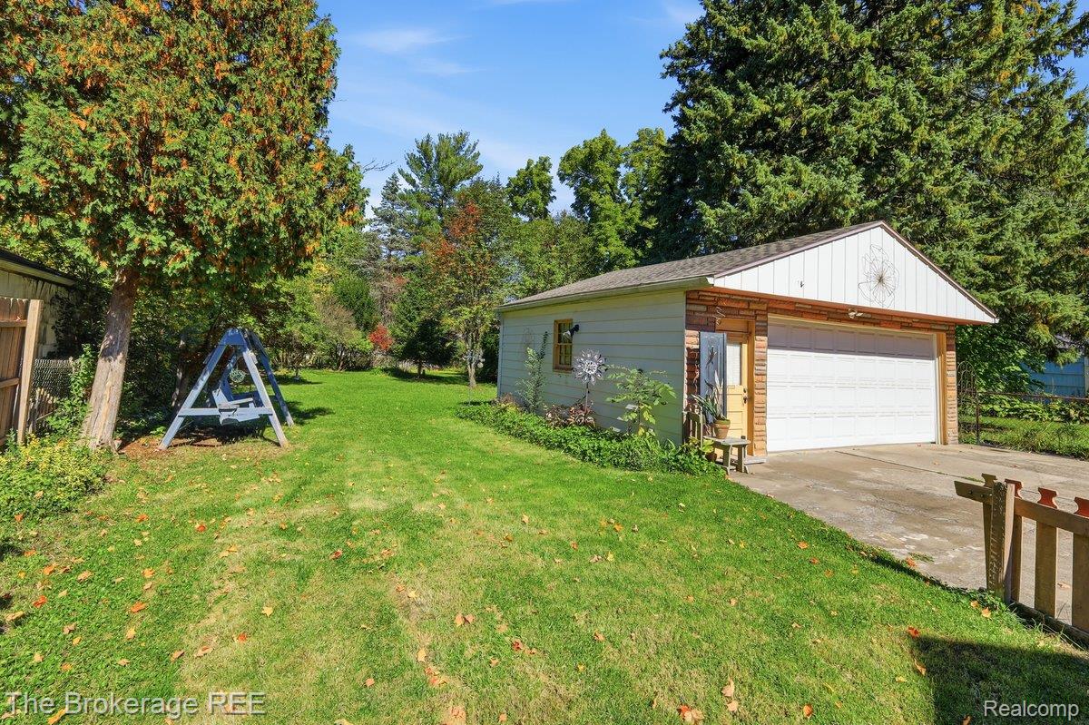613 East Atherton Road Flint, MI 48507 - Photo 31 of 42 Detached garage with a paneled overhead door and side entry, featuring a concrete driveway and surrounding green lawn