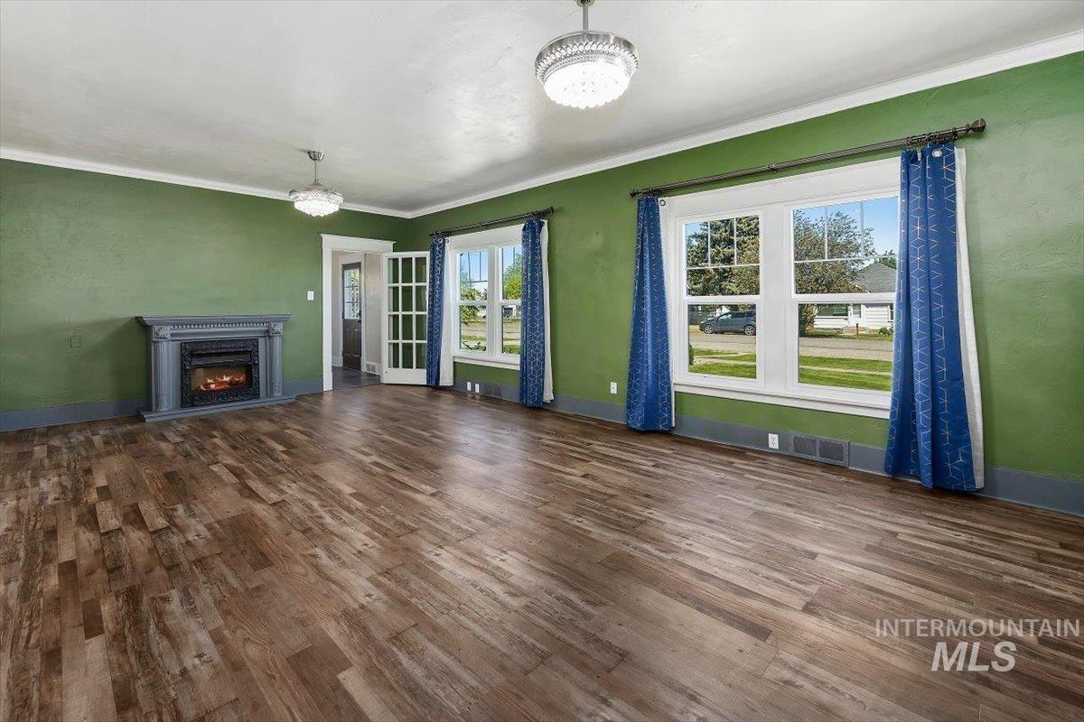 813 7th Street Rupert, ID 83350 - Photo 9 of 48 Spacious interior featuring wood-finish flooring, a decorative fireplace with a gray mantel, two large windows, a pair of French doors, and two crystal-style ceiling light fixtures