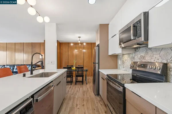 a kitchen with stainless steel appliances a sink a stove top oven a chimney cabinets and wooden floor