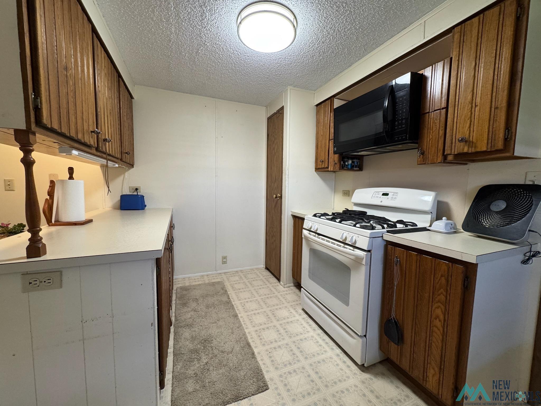 6660 Cherokee Road Dexter, NM 88230 - Photo 10 of 46 Kitchen featuring wood-finish cabinetry, white countertops, a white gas range, and a black over-the-range microwave