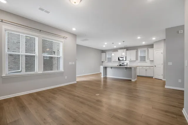 a view of an empty room with wooden floor and a kitchen