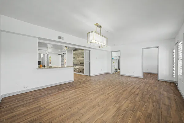 a view of empty room with wooden floor and kitchen