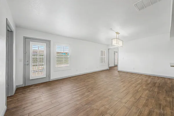 an empty room with wooden floor chandelier and windows
