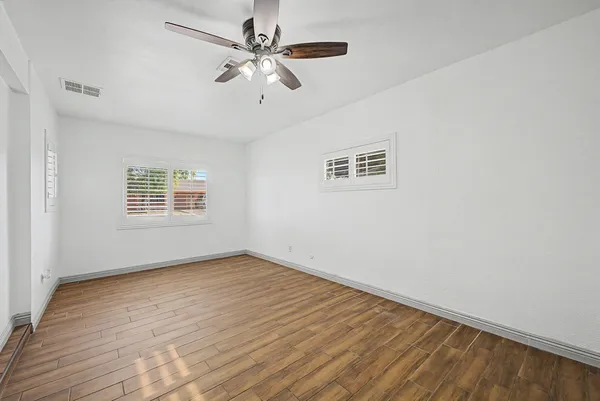 an empty room with wooden floor chandelier fan and windows