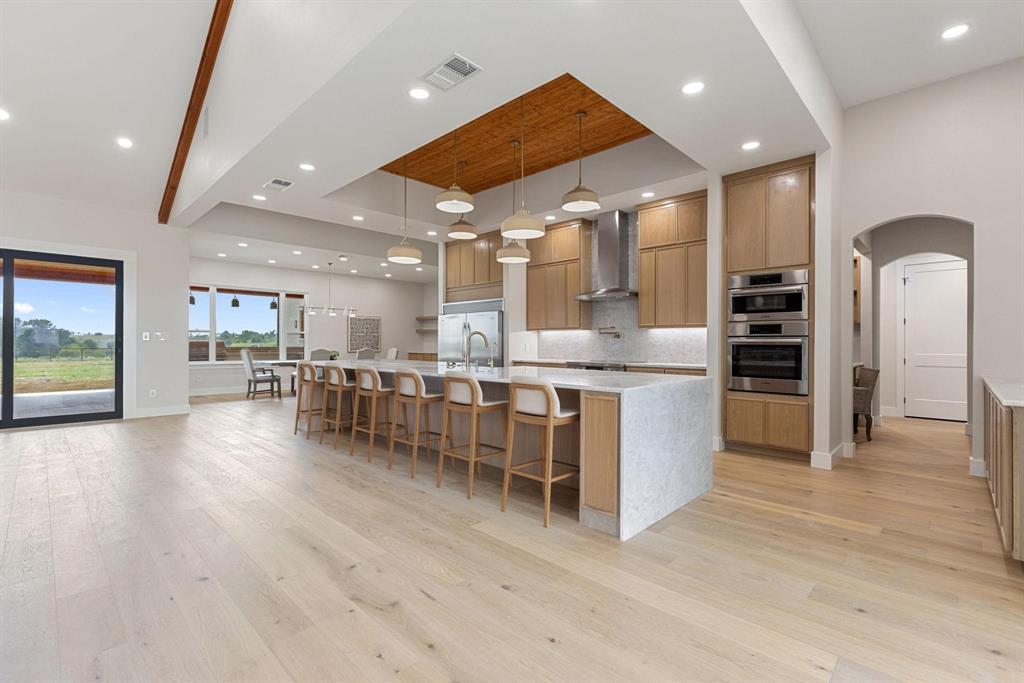 6505 County Road 1126B Godley, TX 76044 - Photo 7 of 39 Kitchen featuring a tray ceiling, arched walkways,light stone countertops, a large island with sink,and hanging light fixtures