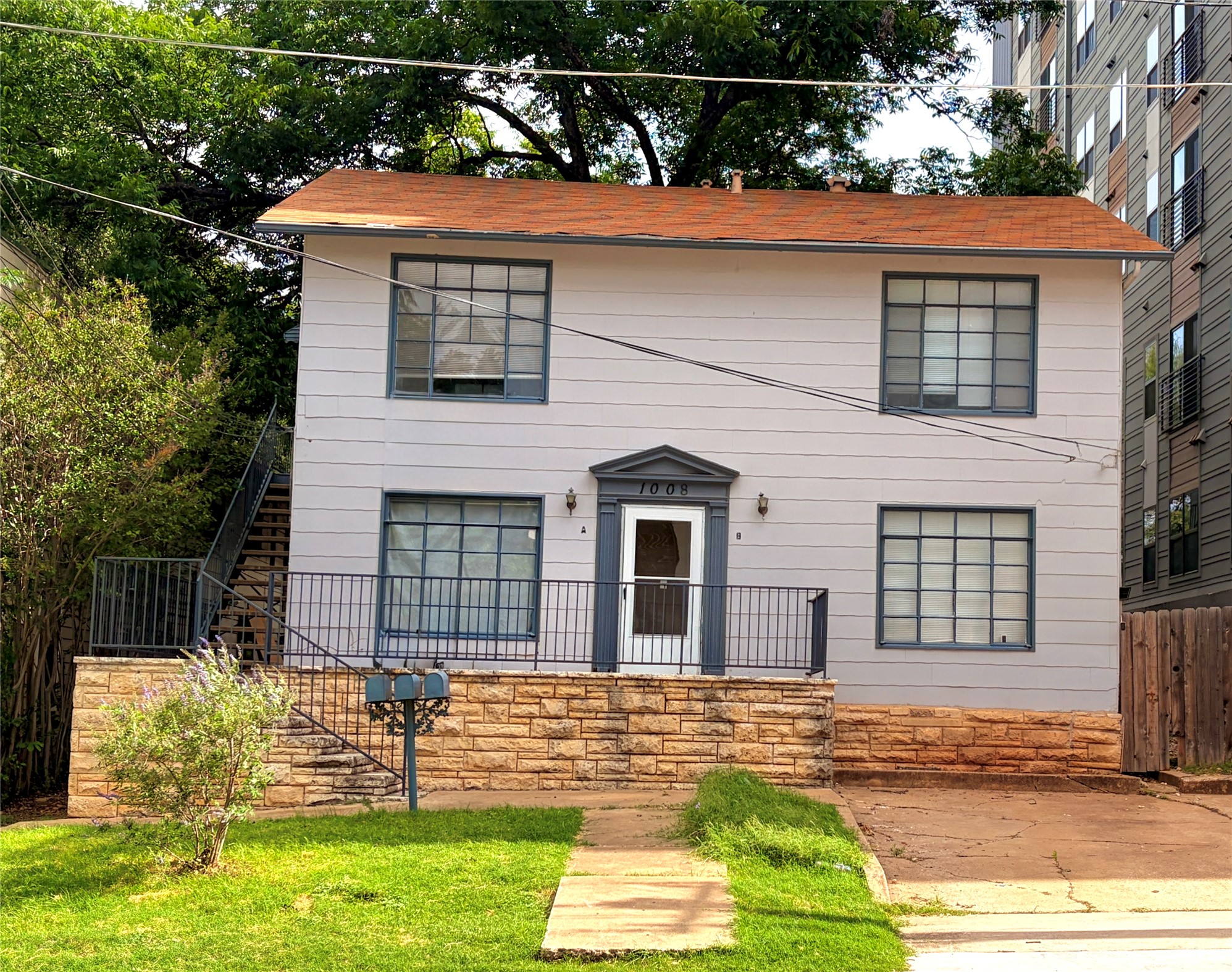 1008 West 25th Street, Unit A Austin, TX 78705 - Photo 1 of 1 Two-story residence featuring a light gray exterior, a prominent orange-red shingle roof, and multiple large grid-style windows