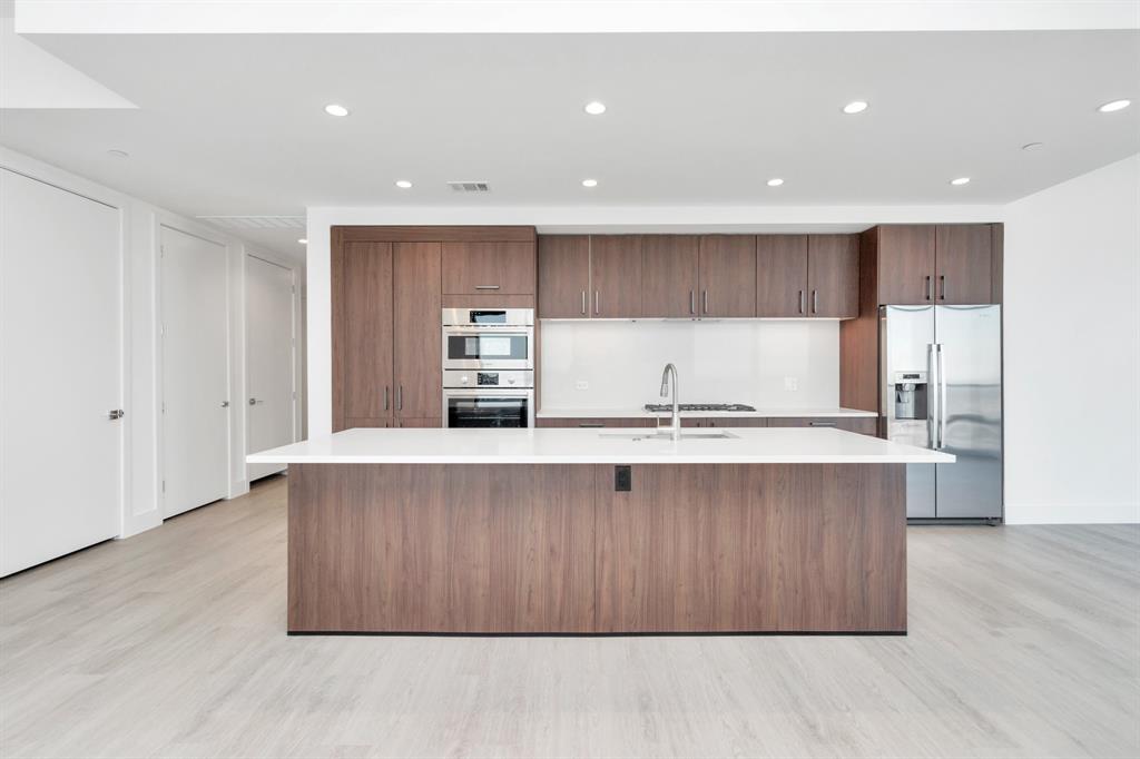 a large kitchen with stainless steel appliances a large counter top a wooden floors and a large window