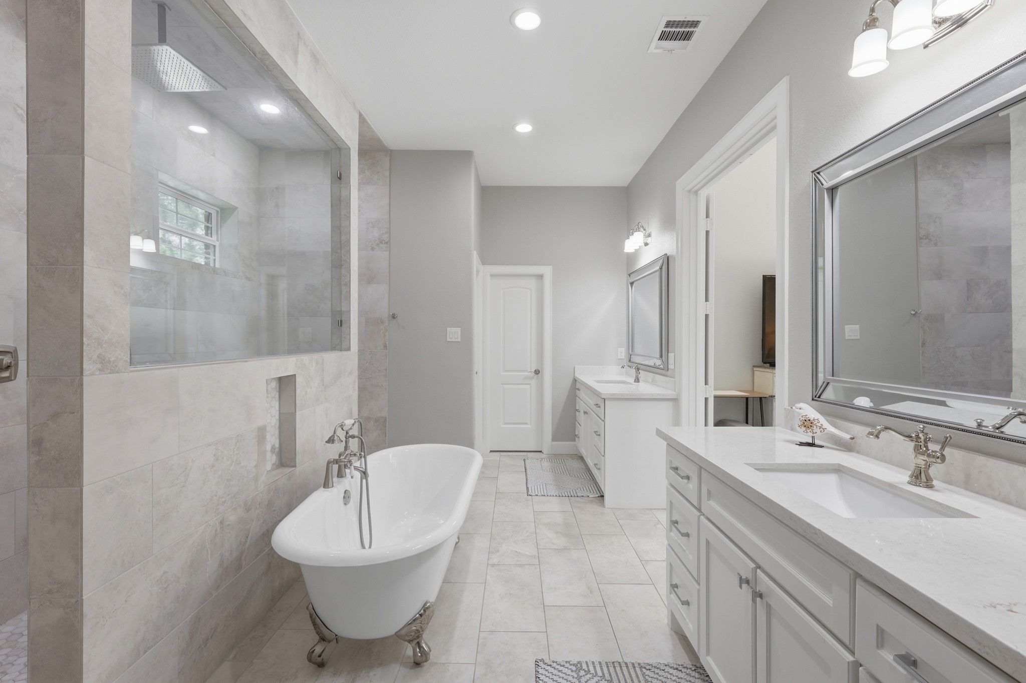 7106 Hampton Court Spring, TX 77389 - Photo 12 of 31 This is a spacious, modern bathroom featuring a freestanding bathtub, a large walk-in shower with glass enclosure, dual sinks with elegant fixtures, and ample cabinetry. The neutral color palette and recessed lighting create a bright, inviting atmosphere.
