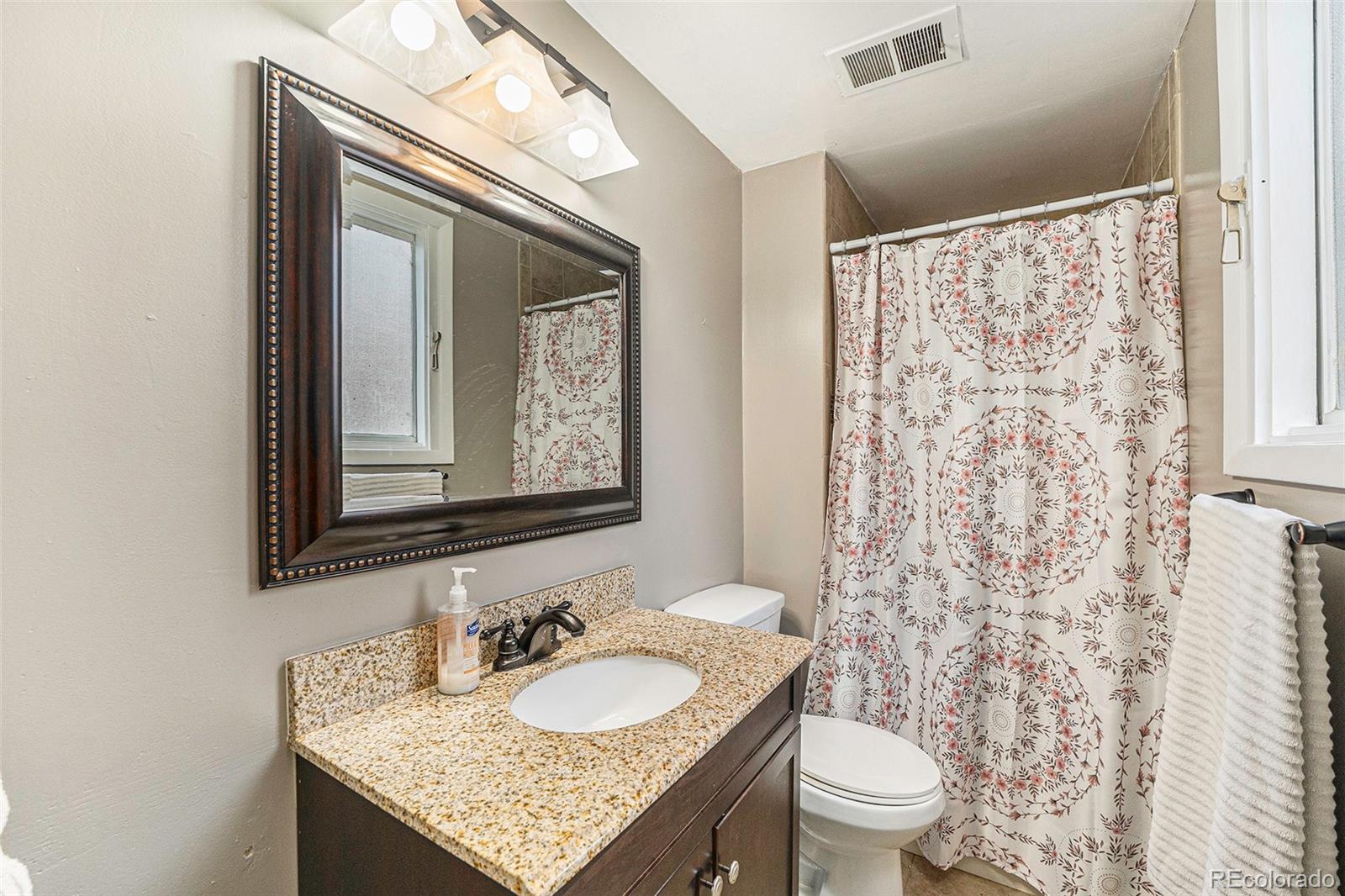 2872 South Gray Way Denver, CO 80227 - Photo 23 of 35 a bathroom with a granite countertop toilet a sink a mirror and a shower curtain