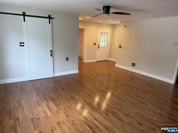 a view of an empty room with wooden floor and a ceiling fan
