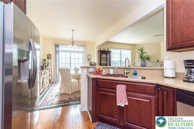 a kitchen with stainless steel appliances granite countertop a refrigerator a sink dishwasher a stove and a dining table with wooden floor