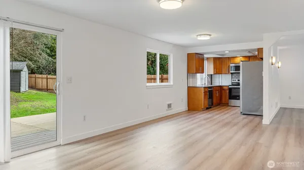 an empty room with wooden floor kitchen view and a window