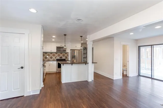 a kitchen with stainless steel appliances granite countertop a refrigerator a stove a sink and white cabinets with wooden floor