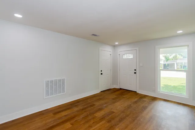 a view of an empty room with wooden floor and a window
