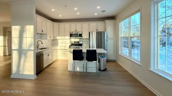 a kitchen with stainless steel appliances kitchen island granite countertop a refrigerator a stove top oven and a dining table with wooden floor