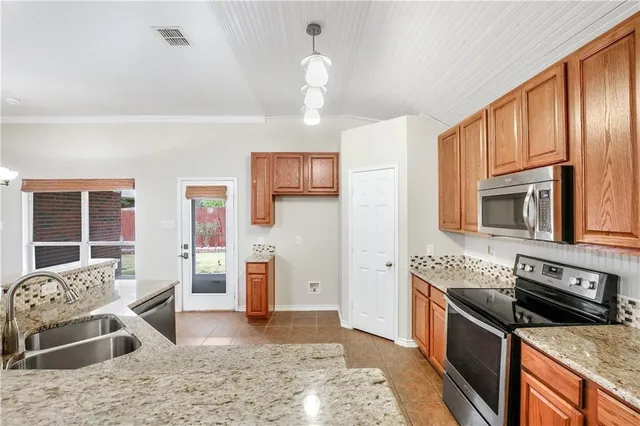 a large kitchen with granite countertop a large counter top cabinets appliances and a chandelier