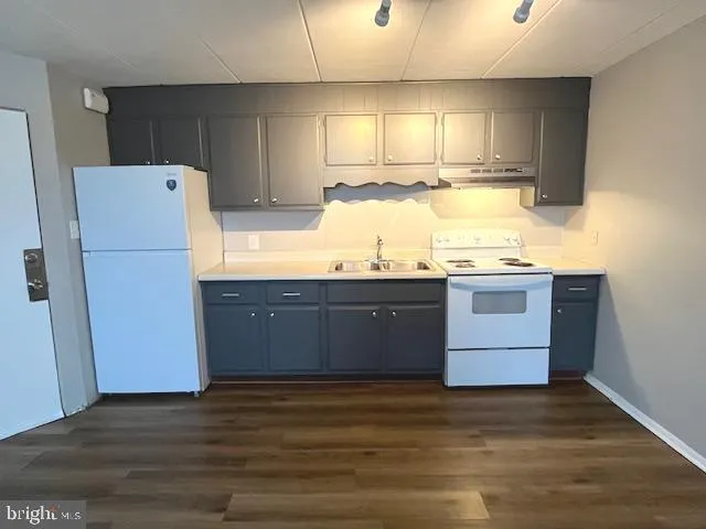 a kitchen with granite countertop a refrigerator a sink and wooden floors