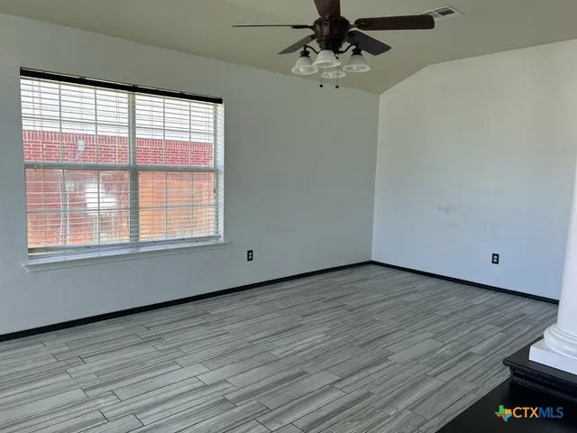 a view of an empty room with wooden floor and a window