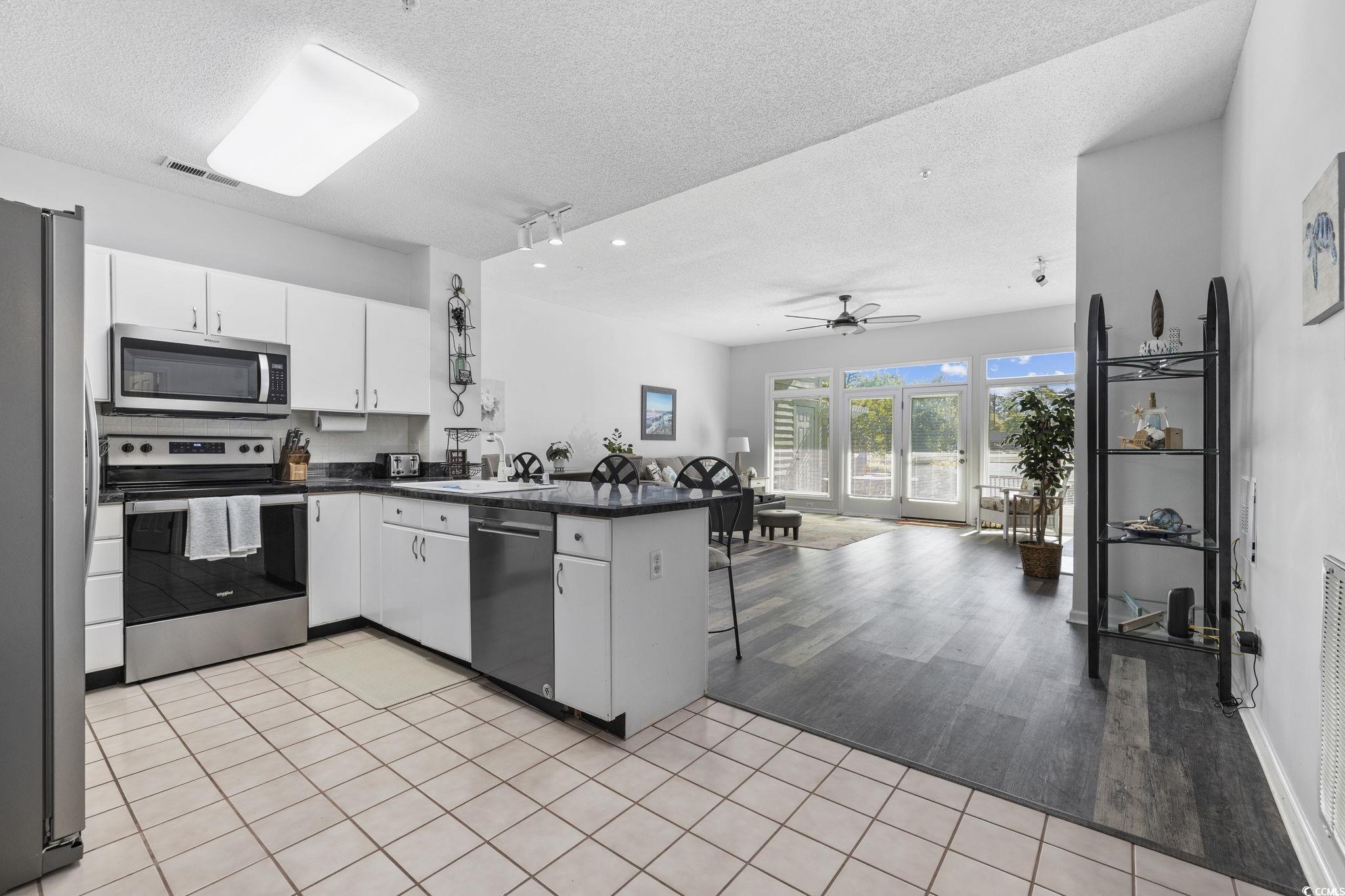 1221 Tidewater Drive, Unit 412 North Myrtle Beach, SC 29582 - Photo 3 of 36 Kitchen with a peninsula, appliances with stainless steel finishes, white cabinetry, a ceiling fan, and a textured ceiling