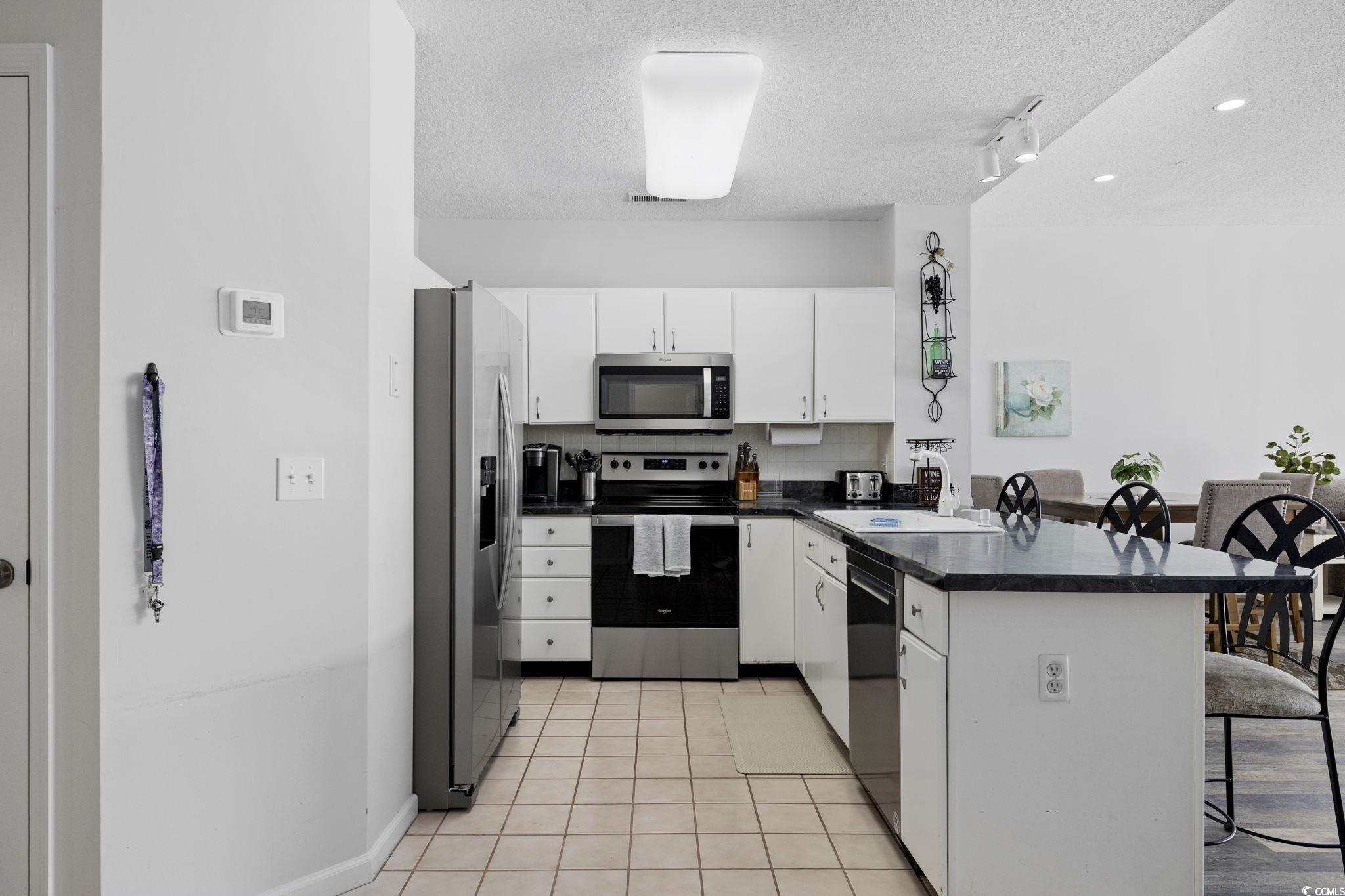 1221 Tidewater Drive, Unit 412 North Myrtle Beach, SC 29582 - Photo 4 of 36 Kitchen with a breakfast bar area, a peninsula, appliances with stainless steel finishes, a textured ceiling, and light tile patterned floors