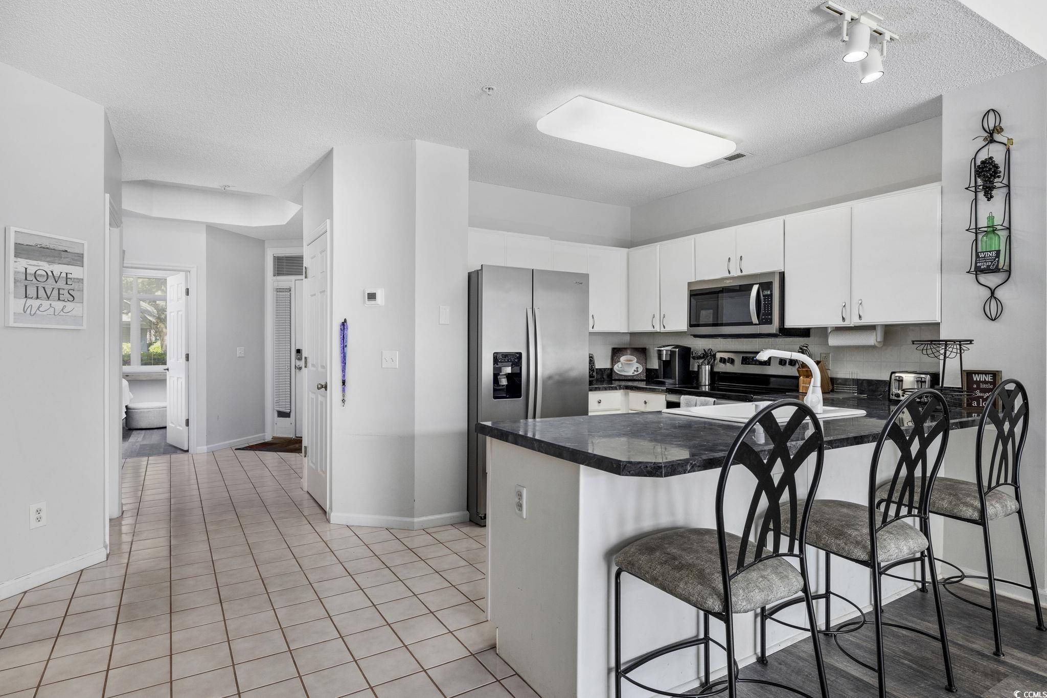 1221 Tidewater Drive, Unit 412 North Myrtle Beach, SC 29582 - Photo 6 of 36 Kitchen featuring a textured ceiling, white cabinets, a peninsula, a kitchen bar, and light tile patterned floors