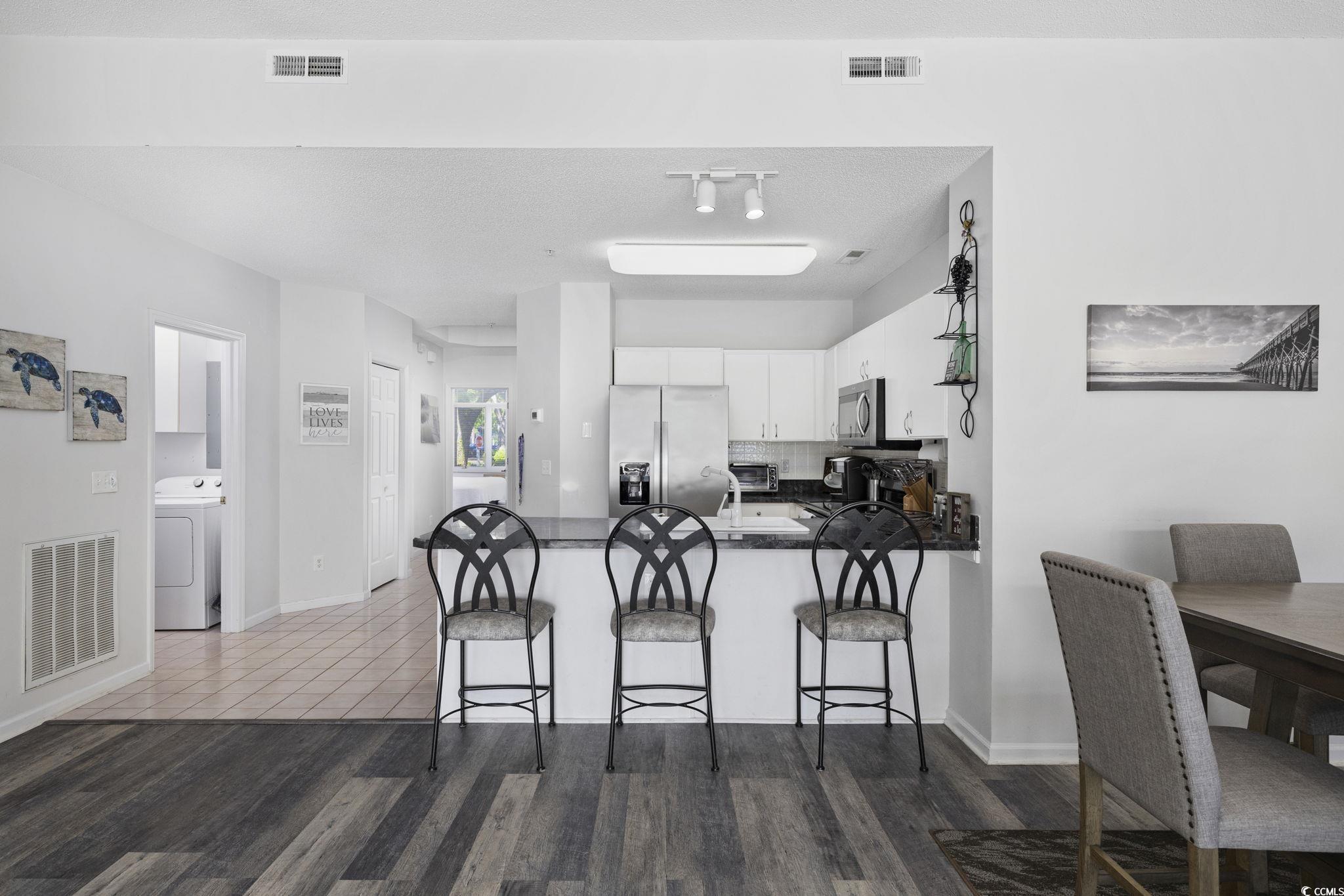 1221 Tidewater Drive, Unit 412 North Myrtle Beach, SC 29582 - Photo 8 of 36 Kitchen featuring a peninsula, white cabinets, stainless steel fridge, washer / dryer, and dark wood-type flooring