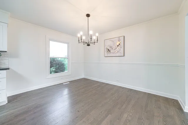 an empty room with wooden floor chandelier and windows