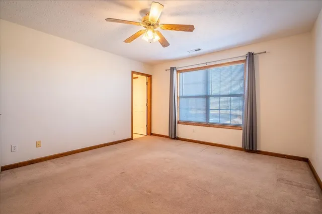 an empty room with chandelier fan and windows