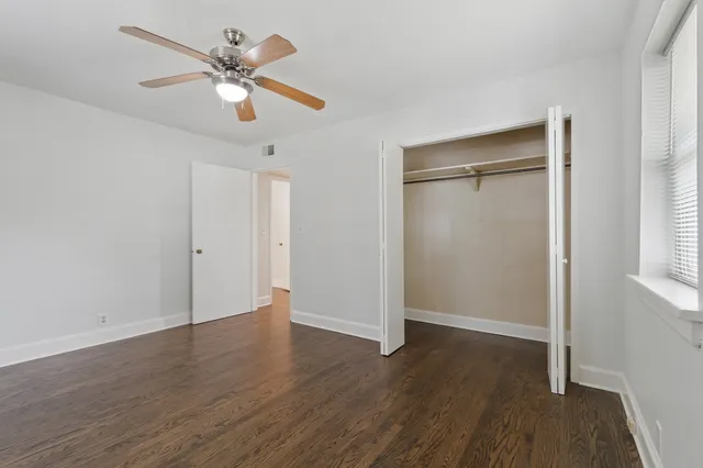 an empty room with wooden floor fan and windows
