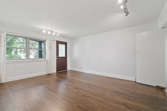 a view of an empty room with wooden floor and a window