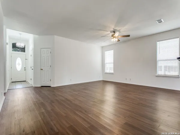 an empty room with wooden floor chandelier fan and windows