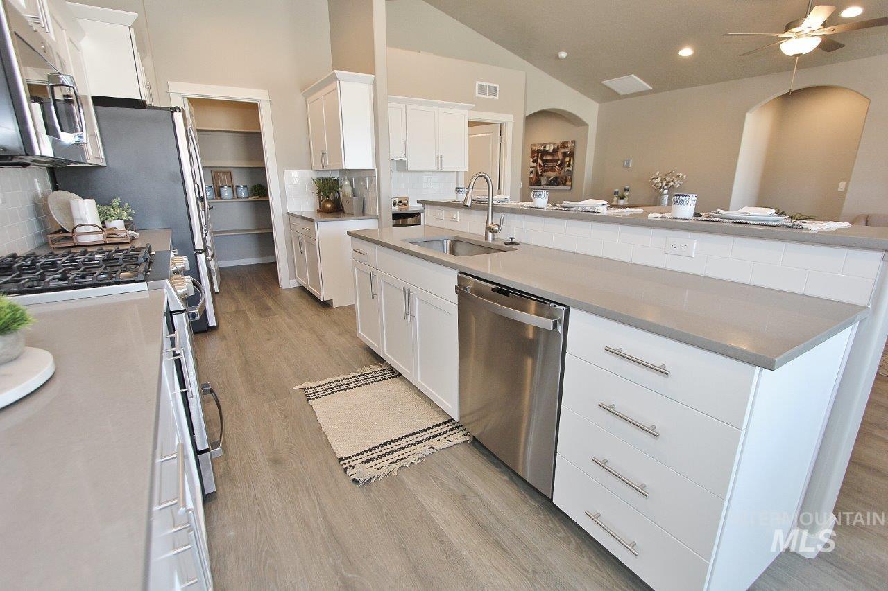 Kitchen featuring white cabinets, backsplash, appliances with stainless steel finishes, light wood finished floors, and vaulted ceiling