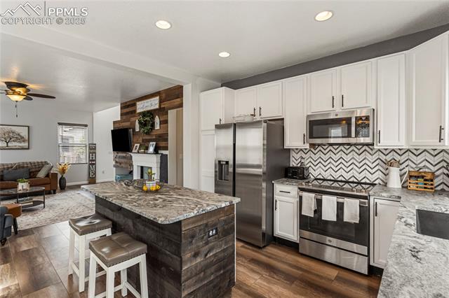 10158 Angeles Road Peyton, CO 80831 - Photo 43 of 43 Kitchen featuring tasteful backsplash, open floor plan, white cabinets, light stone countertops, and appliances with stainless steel finishes