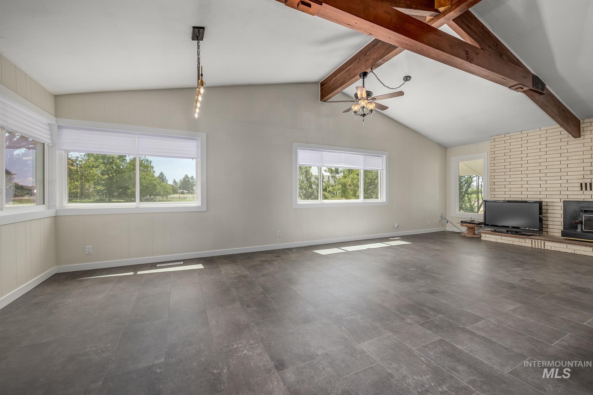 748 Pringle Road Weiser, ID 83672 - Photo 5 of 47 Spacious room featuring vaulted ceilings with exposed wood beams, wood-finish flooring, a brick fireplace with hearth, and multiple windows