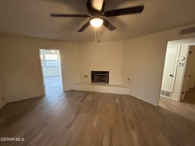 an empty room with wooden floor chandelier fan and windows